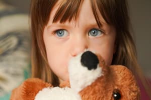 child hugging teddy bear looking worried