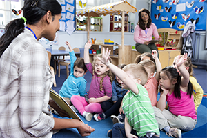 practitioner reading storybook to children and children raising their hands