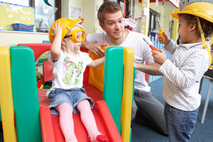 practitioner talking to children while they play on a slide