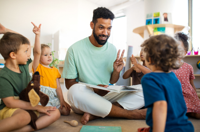 Man reading story on floor with children at nursery