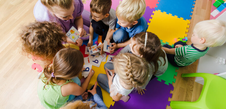 Group of kindergarten kids sitting closely on a floor together with teacher, providing group work. Children learning to cooperate while solving tasks.